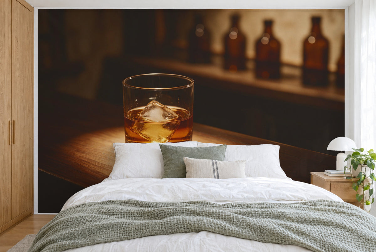 Tela impresa XXL: vaso de whisky con un cubito de hielo a la izquierda, botellas marrones detrás, pared entera tras la cama