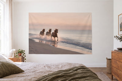 Wild Horses on the Beach tapestry in a bright bedroom opposite the bed, wooden dresser at right – peach and gray