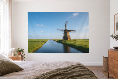Wandtuch Windmühle am Kanal im hellen Schlafzimmer gegenüber dem Bett, rechts eine Holzkommode – Blau und Grün