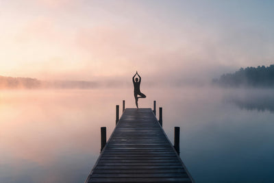 Yoga silhouette in tree pose on a wooden jetty by a misty lake under the rising sun, tapestry printed on fabric
